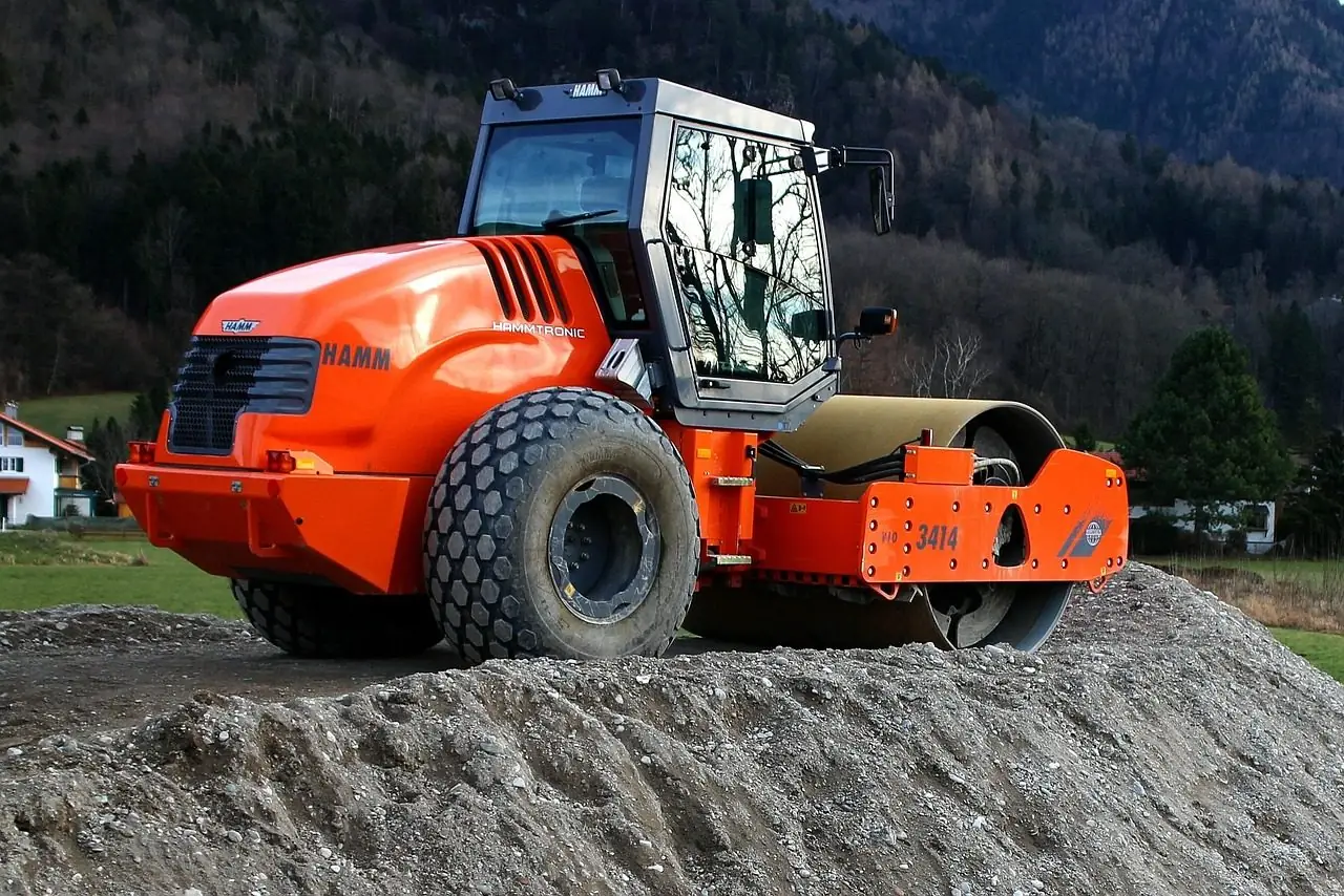 Orange vibratory roller parked on a pile of gravel