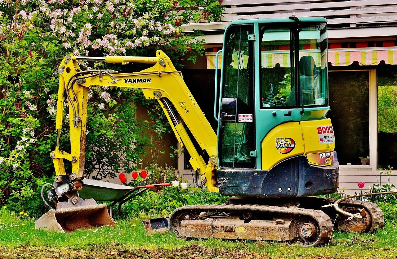 Yellow mini excavator working in a garden beside flowers